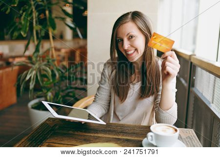 Woman Sitting Near Big Window In Coffee Shop At Table With Credit Card, Cup Of Coffee, Cake, Relaxin
