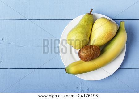 Top View On Wooden Ristic Table With Pile Ripe Fruit On White Plate. Pears, Banana And Kiwi Fruit Fo
