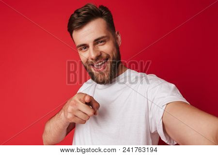 Picture of handsome young man standing isolated over red wall background make a selfie looking camera pointing.