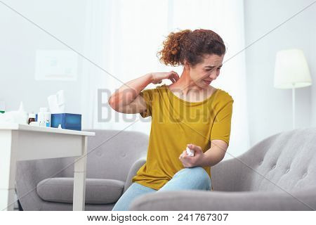 Sore Neck. Young Woman Sitting On A Grey Couch Suffering From A Painful Neck Sprain Giving Her Troub