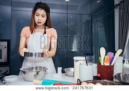 An Asian Woman Is Sifting Flour Into A Bowl. Girl Is Sifting Flour To Making The Bakery In Her Kitch