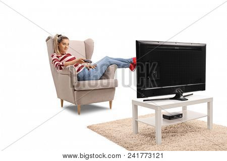 Young woman seated in an armchair watching television and changing channels isolated on white background