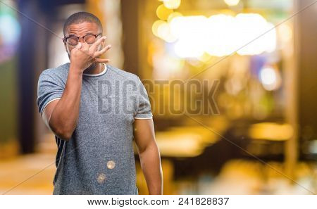 African american man with beard with sleepy expression, being overworked and tired, rubbes nose because of weariness at night