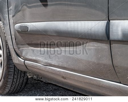 Close up detail of a dented driver door from a car crash or automobile accident. Bent and distorted metal with large dent and body paint scratched