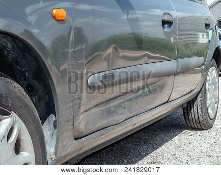 Close up detail of a dented driver door from a car crash or automobile accident. Bent and distorted metal with large dent and body paint scratched