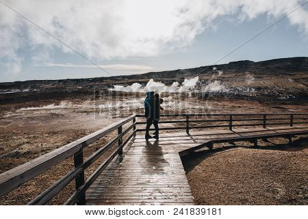 Young Couple Hugging On Wooden Walkway Near Magnificent Hot Springs In Iceland, Reykjanes, Gunnuhver
