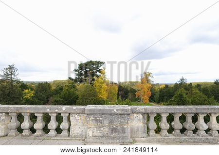 Girl Sitting On Concrete Railing With Green Trees Background. Concept Of Architectural Elements.