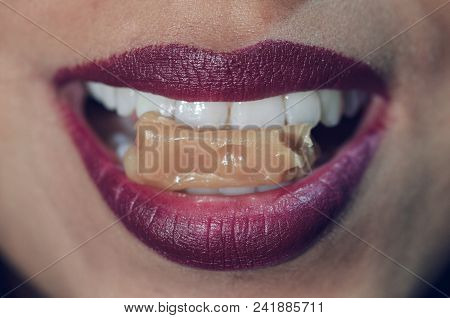 Close-up Of Woman Mouth Biting Caramel Candy With Red Lips