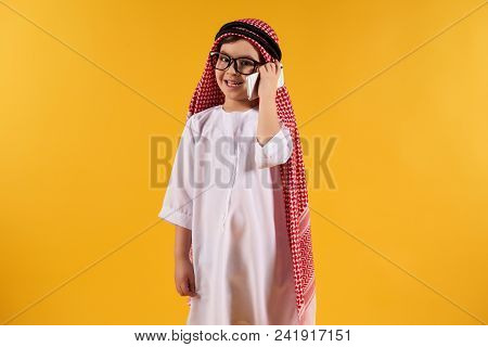 Arab Smart Boy In Kufiya Talking On Smartphone. Isolated On Yellow Background. Studio Portrait.