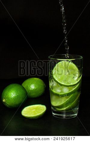 Cold Detox Water With Ice And Fresh Ripe Slice Green Limes On Black Background. Summer Refreshing An