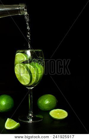 Stream Of Cold Water From A Bottle Is Poured Into A Wineglass To Make Cold Drink With Ice And Fresh 