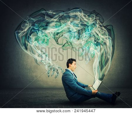 Surprised Businessman Sitting On The Floor Looks At His Laptop As Dark Smoke Comes Out Of The Monito