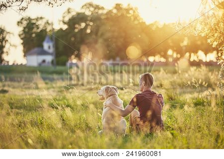 Rear View Of Young Man With Dog (labrador Retriver) In Nature At Sunset.