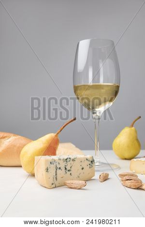 Close Up View Of Dorblu Cheese, Wine Glass, Pears, Almond And Baguette On Gray