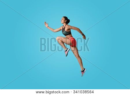 Athletic Young Woman Running On Light Blue Background, Side View
