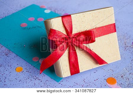 Close Up Of Giftbox Tied With Bright Red Color Ribbon On Purple Background With Sparklets And Confet