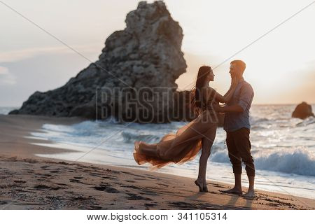 Couple In Love At Dawn By The Sea. Honeymoon Trip. Man And Woman Traveling. Happy Couple By The Sea 