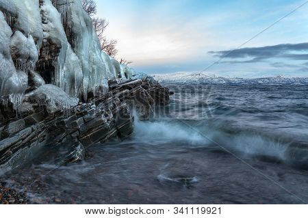 Icicles Hanging From The Rocks On The Shore Tornetrask, Sweden. Beautiful Waves. Long Shutter Speed
