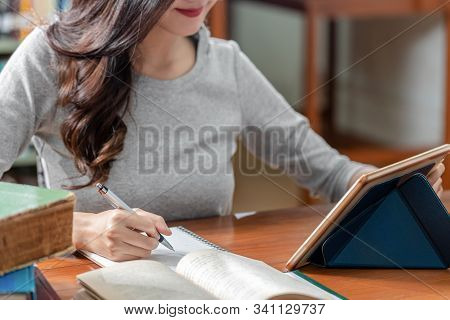Closeup Asian Young Student Hand Writing Homework And Using Technology Tablet In Library Of Universi