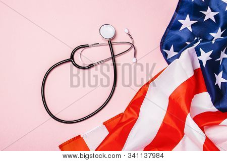 Medical Stethoscope And Us Flag On A Pink Background. Concept Of Health Care, Medicine, Virus, Epide