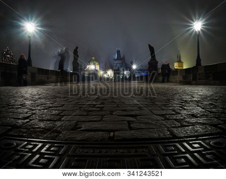 Long Exposure Of Charles Bridge In Prague At Night With Motion Blurred Ghosts Of People Visible. Gro