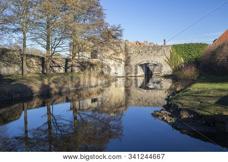 Reflections Of The Ramparts And Trees In Bergues, Northern France, Against A Blue Sky.