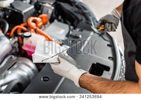 Cropped View Of Mechanic Wiping Oil Dipstick With Rag Near Car Engine Compartment