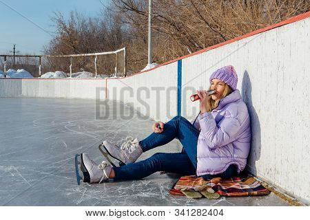 Lovely Young Woman Relaxing After Riding Ice Skates And Drinking Hot Drink From Termo Pot On The Ice