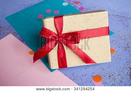 Close Up Of Giftbox Tied With Bright Red Color Ribbon On Purple Background With Sparklets And Confet