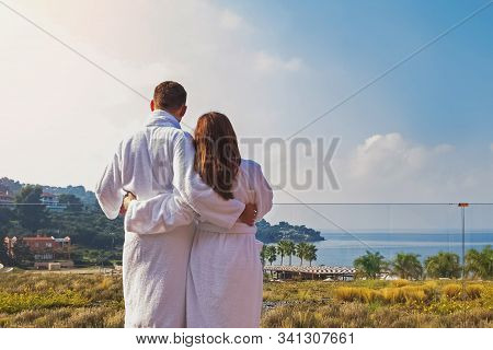 Man And Woman Couple In White Bathrobes Stnding On The Balcony Of Luxury Hotel