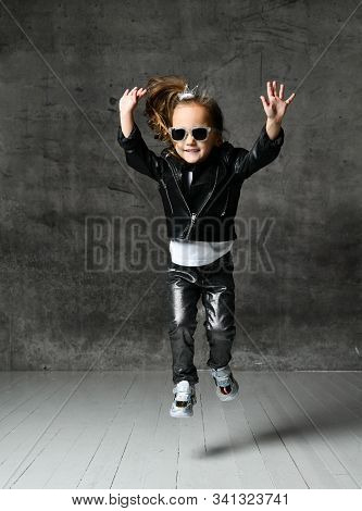 Cheerful Frolic Kid Girl In Leather Jacket, Stylish Jeans And Sunglasses Is Having Fun Playing Jumpi