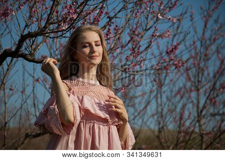 Beautiful Blonde Woman In Pink Dress Walks Through The Flowering Garden Spring