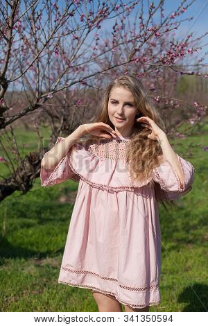 Beautiful Blonde Woman In Pink Dress Walks Through The Flowering Garden Spring
