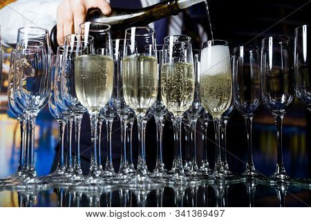 Champagne Is Poured Into Empty Glasses That Stand On A Glass, Transparent Table.