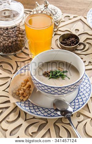 Bowl Of Mushroom Cream Soup With Croutons And Glass Of Yellow Drink On Oriental Wooden Table