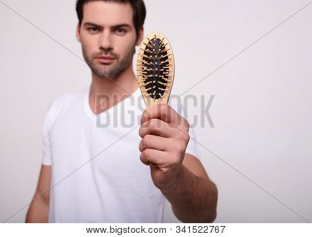 A Confident Young Handsome Guy With Dark Hair In A White T-shirt Shows The Camera A Wooden Comb. The