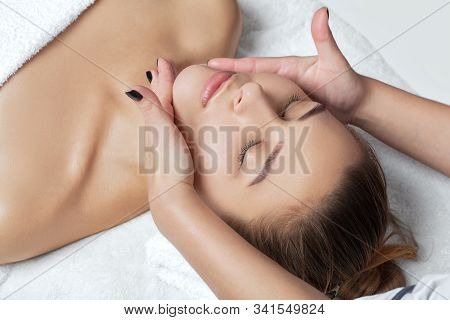 Masseur Makes A Relaxing Massage On The Face, Neck, Shoulders And Collarbones Of A Young Beautiful W