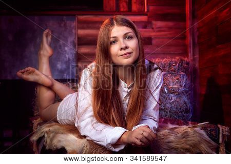 Beautiful Girl In White Shirt On The Couch With Hay In The Barn Or In The Hayloft With Wooden Walls.