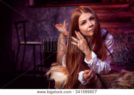 Beautiful Girl In White Shirt On The Couch With Hay In The Barn Or In The Hayloft With Wooden Walls.