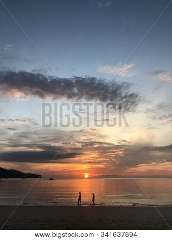 Man And Woman Are Waliking Into The Scene Of Golden Sunset Light With Amazing Twilight Sky And Yacht