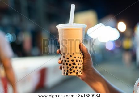 Asian woman holding the famous taiwanese bubble milk tea at night marketplace