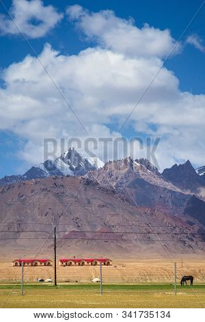 Majestic Snow-capped Mountains Peak With Cloudy Blue Sky In Pamirs Plateau,alone Black Horse Grazing