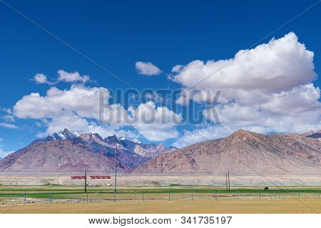 Majestic Snow-capped Mountains Peak With Cloudy Blue Sky In Pamirs Plateau,alone Black Horse Grazing