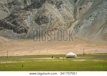 White Mongolian Traditional Yurt And A Woman On Pastures At The Foot Of Rocky Mountain In Pamirs Pla