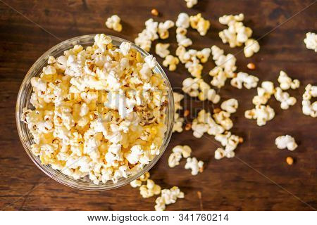 Top View Of Popcorn In A Glass Cup With Popcorn Pread On A Wooden Table.