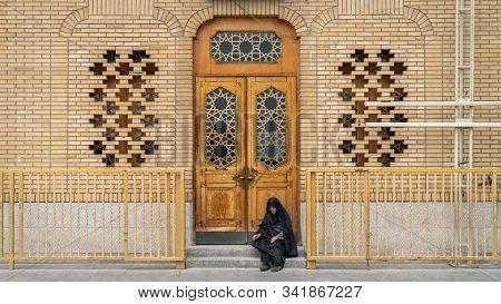 Qom, Iran - May 2019: Iranian Woman Sitting By A Door In The Sacred City Of Qom, Which Is Considered
