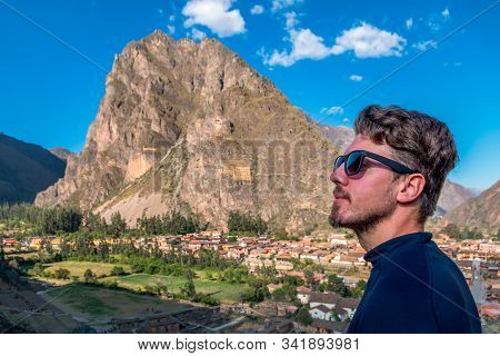 A Man Tourist In Profile With Sun Glasses, With The Background Of The City Of Ollantaytambo, Sacred 