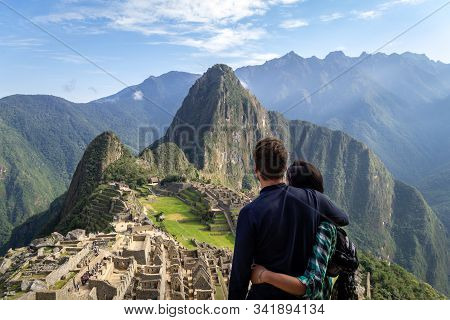 Young Couple Embracing Contemplating The Incredible Landscape Of Machu Picchu. The Ruins Of The Cita