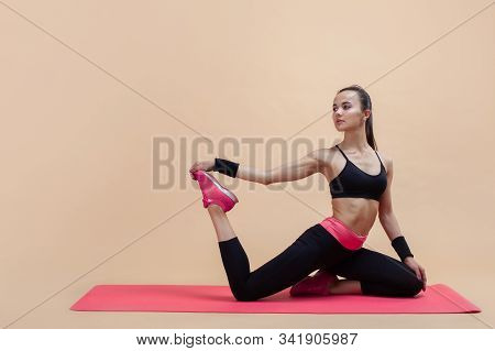 A Young Attractive Girl With A Ponytail, A Brunette, Sits In A Mermaid Pose On A Pink Yoga Mat, On A