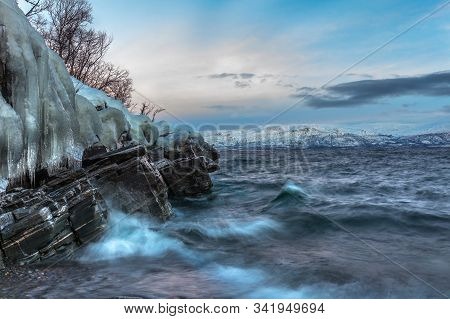 Icicles Hanging From The Rocks On The Shore Tornetrask, Sweden. Beautiful Waves. Long Shutter Speed